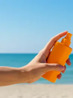 Hand applying sunscreen at a bright US beach, symbolizing summer SPF protection