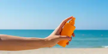Hand applying sunscreen at a bright US beach, symbolizing summer SPF protection